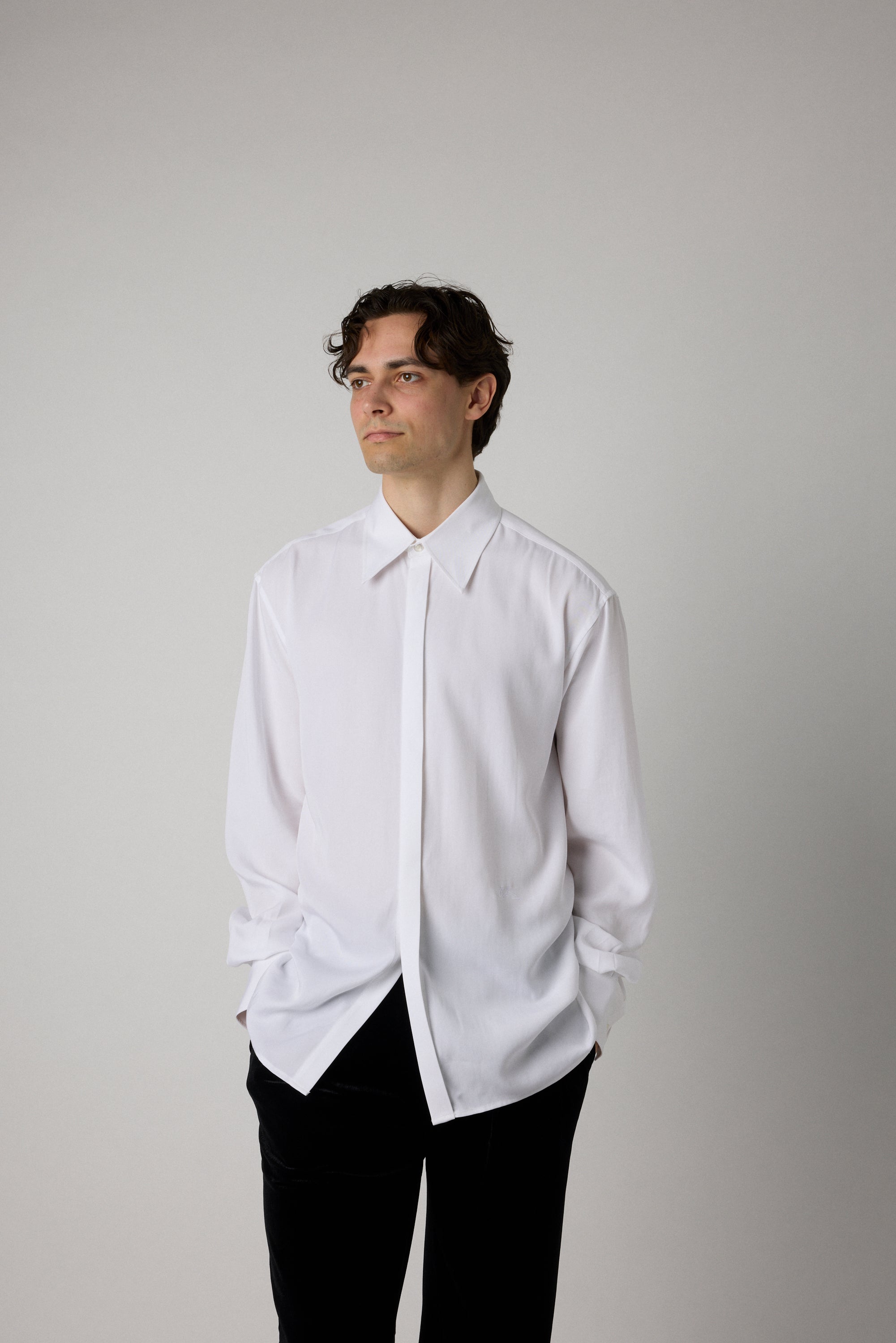 Man wearing a white shirt and black pants against a plain background