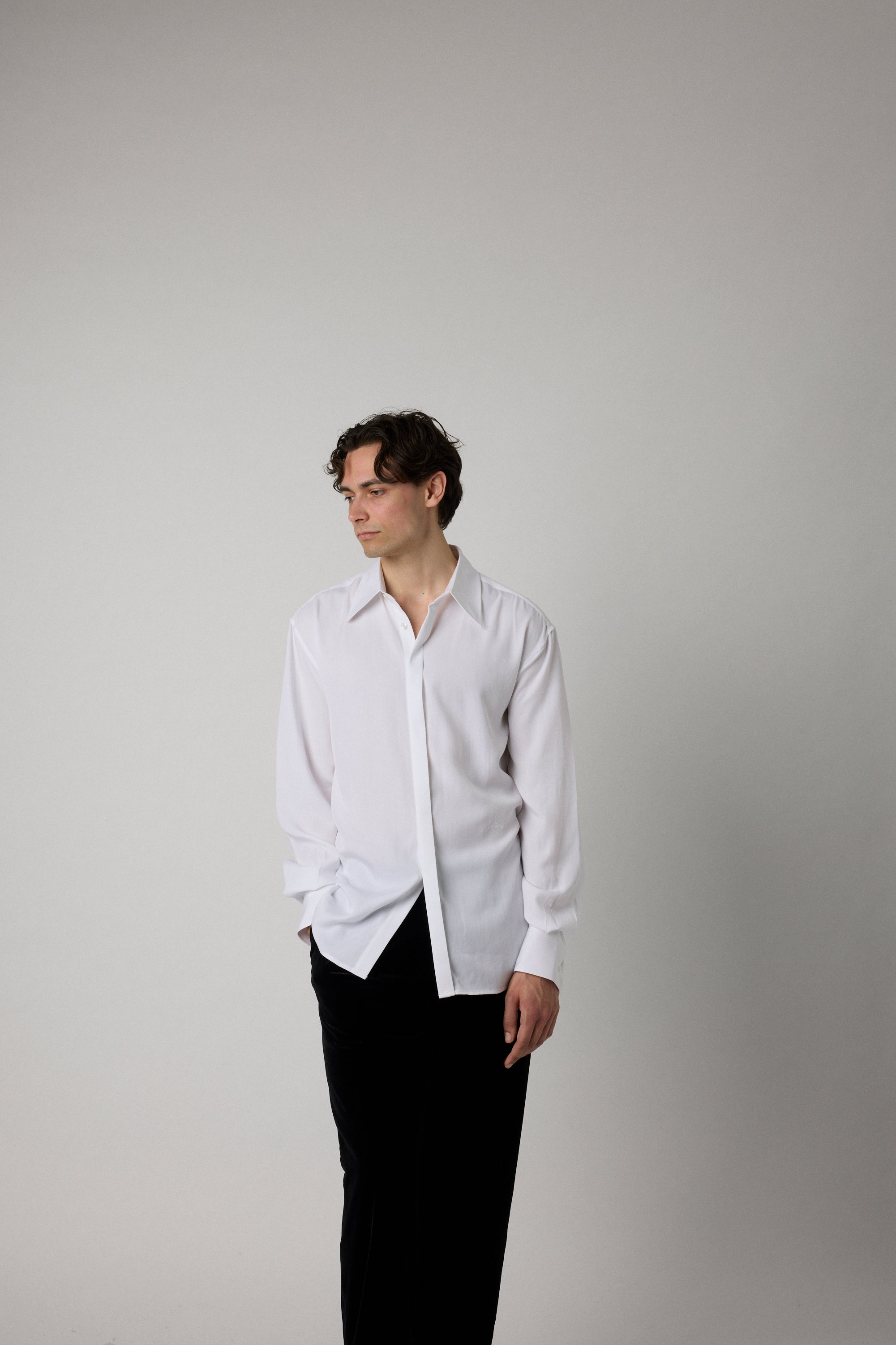 Man wearing a white shirt and black pants against a plain background