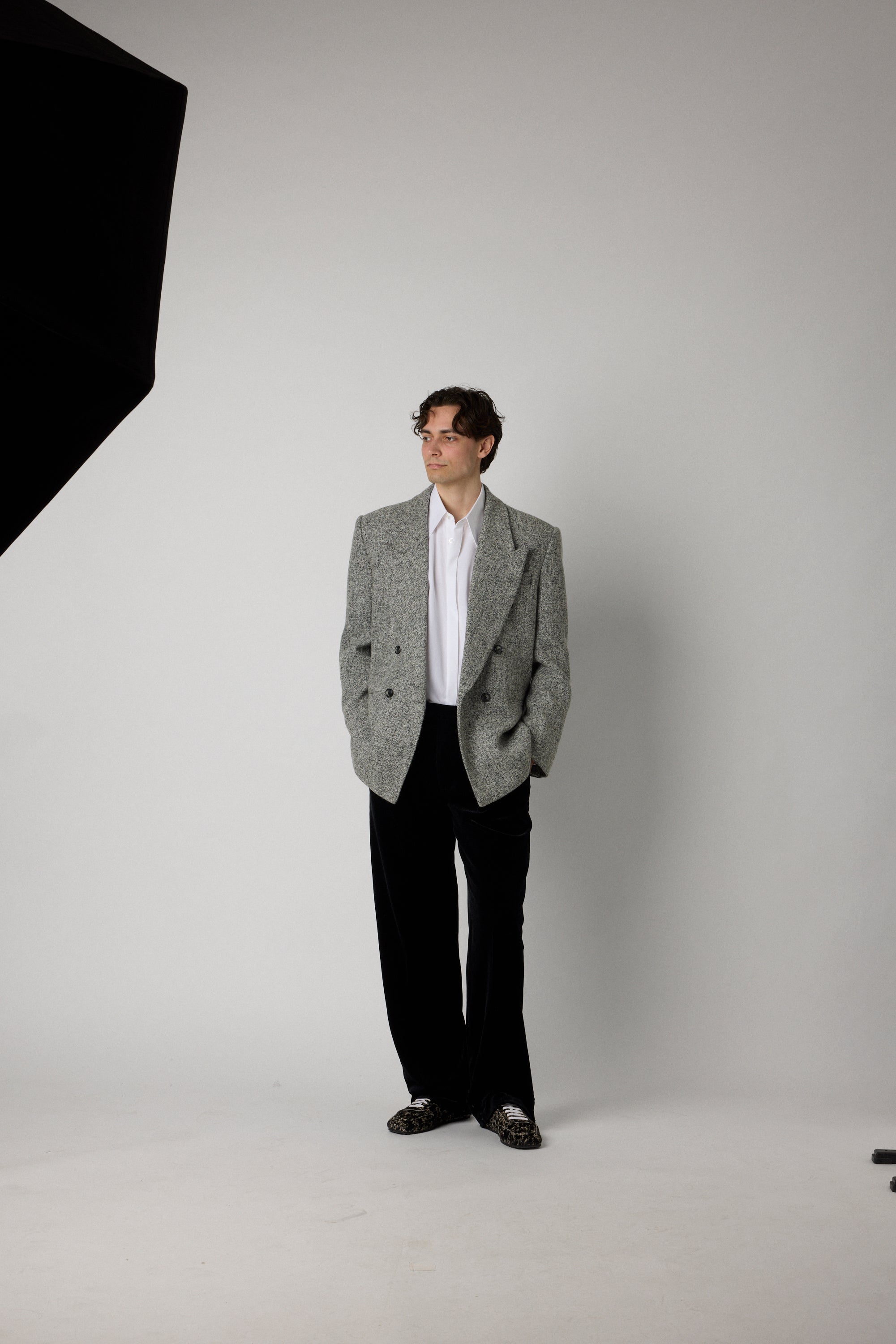 Man wearing a gray blazer and black pants standing against a plain white background